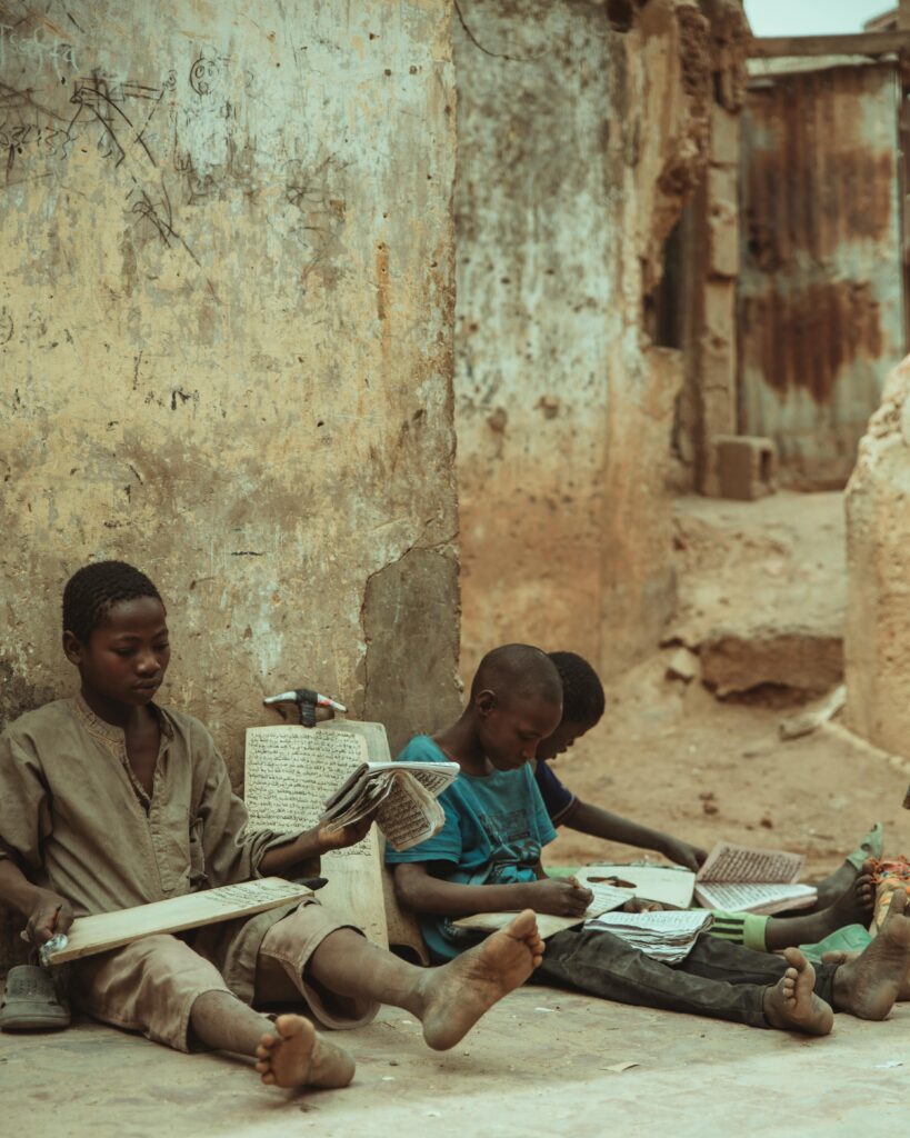 Children sit on city street engaged in reading and learning activities.
